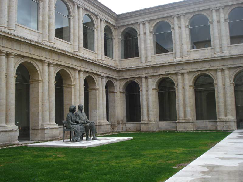 Patio donde se ven ventanas  en forma de arco con dos bustos en el centro del patio de los Reyes eméritos de España