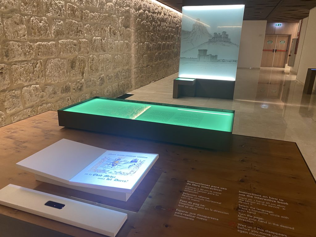 Sala del museo con elementos digitales interactivos (libro y pantallas verticales).