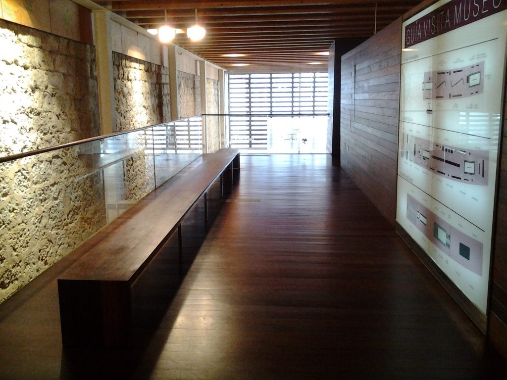 Zona de paso de museo donde vemos un banco de madera a la izquierda y a la derecha paneles informativos