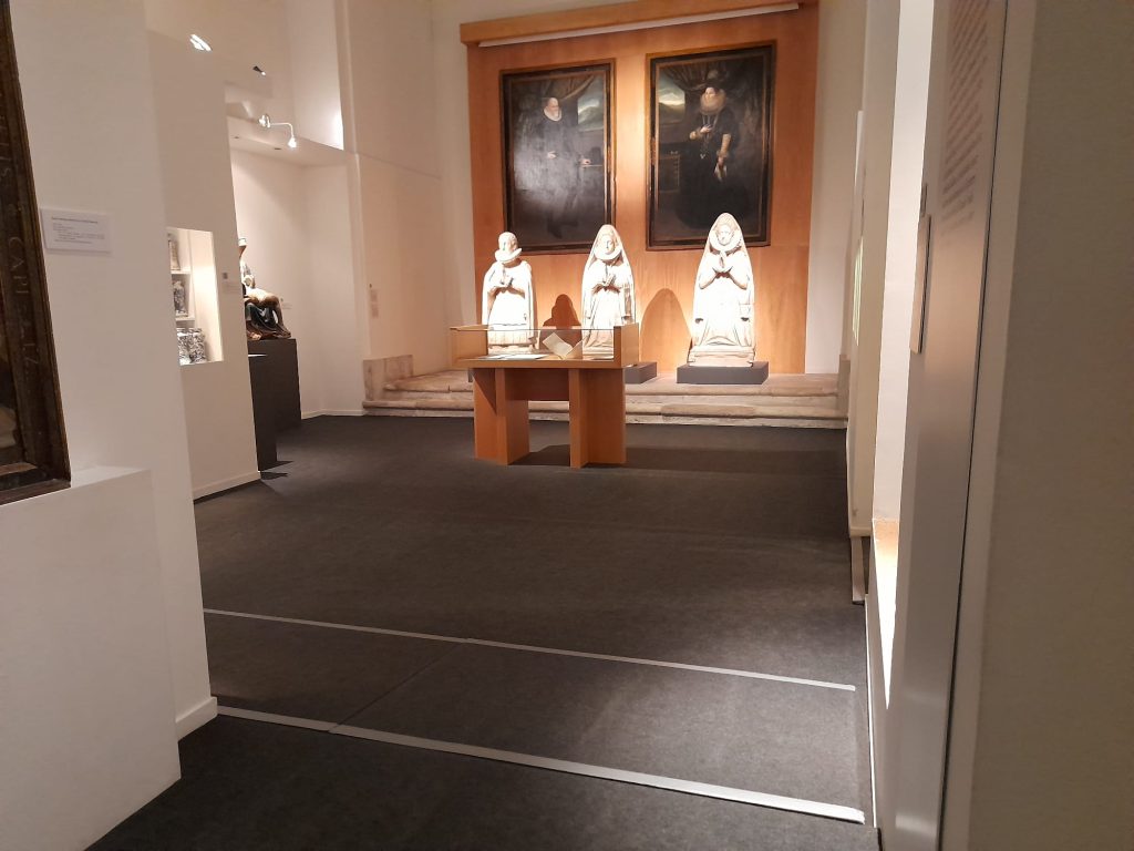 Sala del museo con paredes blancas en la que se pueden ver tres tallas de gran tamaño y dos pinturas colgadas en la pared. 