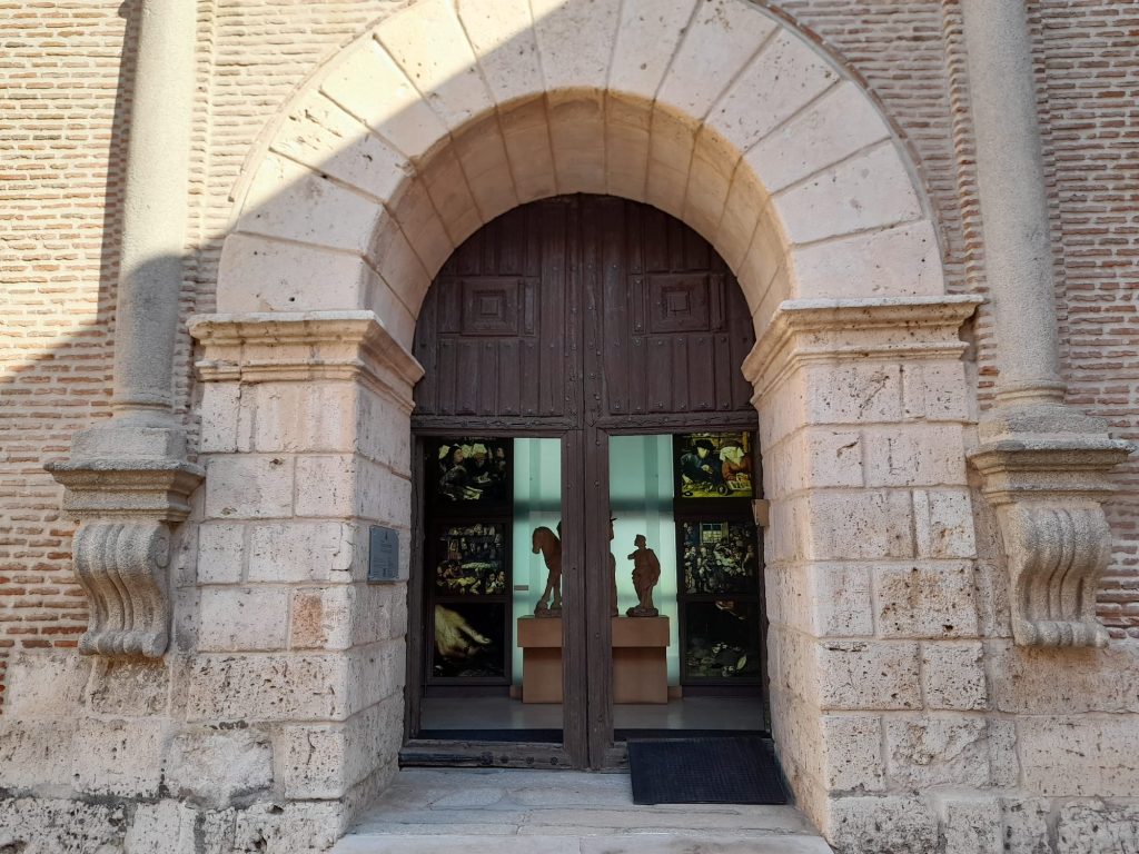 Fachada del edificio y puerta de entrada al museo con arco de piedra entre dos columnas y puerta de madera de doble hoja. Rampa  móvil de acceso. 